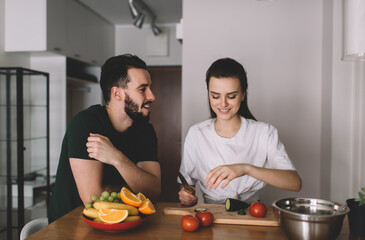 Fototapeta na wymiar Carefree spouse enjoying bonding time on weekend cooking dinner togetherness and smiling at home kitchen, happy male and female 20s communicating while preparing salad of tomato and cucumber