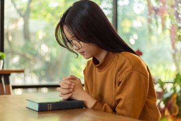 Young Asian Woman Hands folded in prayer on a Holy Bible.