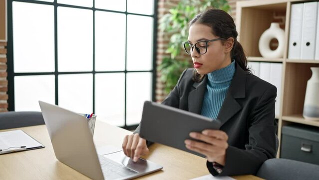 Young beautiful hispanic woman business worker using laptop and tablet at office