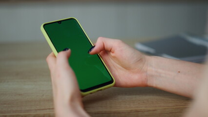 Woman holding greenscreen smartphone scrolling touchscreen at home close up.