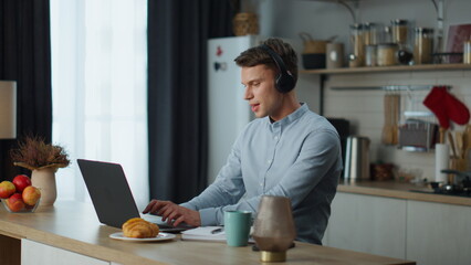 Obraz na płótnie Canvas Freelancer working listening music with headphones sitting at kitchen table.