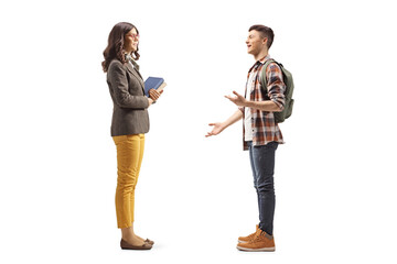 Full length profile shot of a male student talking to a female teacher standing and holding books