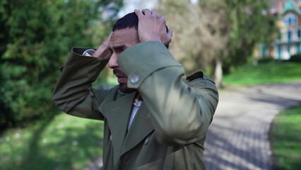 Fototapeta premium Preoccupied man standing outside at park having a regretful memory. Worried person feeling anxiety