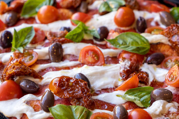 Pizza con pomodori secchi, pomodorini, mozzarella, burrata, basilico e olive, primo piano