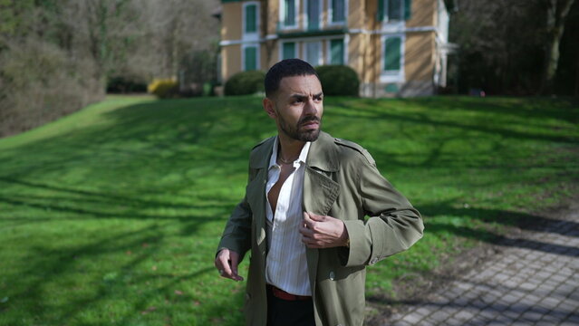 One confident young Middle Eastern man walking outside at park wearing fashionable jacket. An Arab male person with serious expression walks outdoors