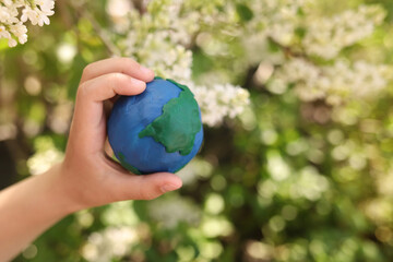 plasticine planet Earth in children's hands on a background of flowers. day earth, save environment concept