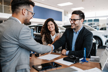 Middle age couple choosing and buying car at car showroom. Car salesman helps them to make right decision. Man signs buyers contract. - obrazy, fototapety, plakaty