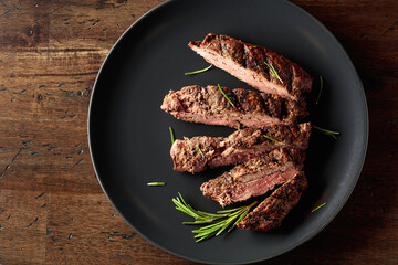 Grilled beef steak with rosemary on a black plate.
