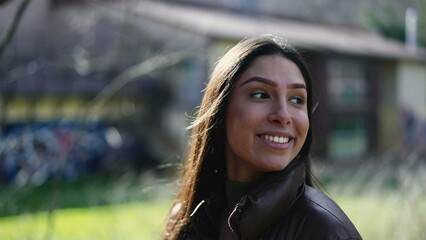 Happy young woman closeup face walking outside in sunlight park with carefree expression. Portrait of a joyful female person in 20s