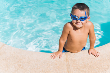 Child on the edge of a pool looking at the camera with diving goggles