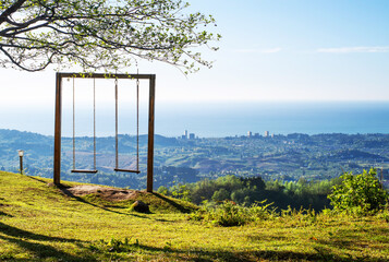 Landscape with a lonely swing on a hill in the mountains overlooking a mountain village, sea, sky on a sunny spring day. Observation platform in the mountains near Batumi