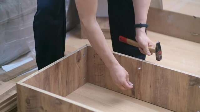 Furniture assembly and repair services specialist hammering shelf holders into wooden cabinet professional carpentry work in apartment in process of renovation