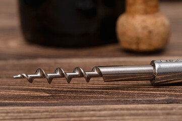 Close-up of corkscrew on table, oak cork and bottle of wine on background