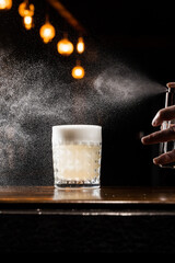 Penicillin classic cocktail in the glass. Bartender is spraying whiskey over Penicillin coctail. Alcohol cocktail with whiskey, lemon juice, and honey-ginger syrup named Penicillin.