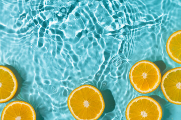 Creative summer background with orange fruit slices in swimming pool water. Summer wallpaper with copy space. - obrazy, fototapety, plakaty