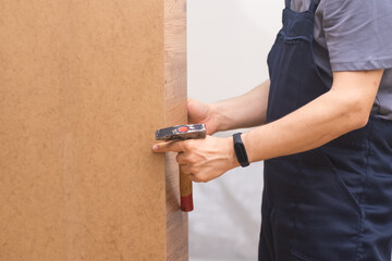Furniture assembly and repair services specialist hammering shelf holders into wooden cabinet professional carpentry work in apartment in process of renovation