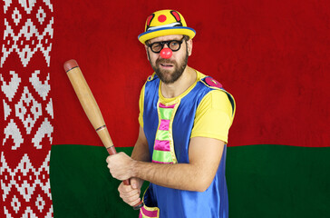 An insecure clown holds a bat in his hands against the background of the flag of Belarus