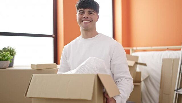 Young hispanic man smiling confident holding package at new home