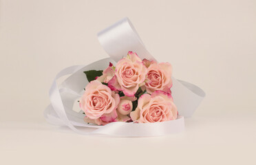 Pink rose flower bouquet with white silk ribbon. Light beige copy space background.
