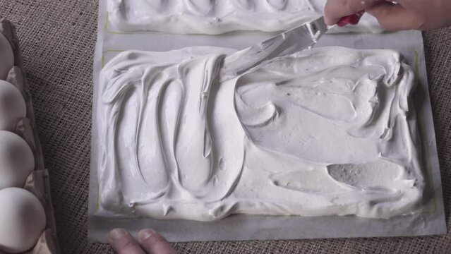 Close up zoom out of pastry chef's hand molding creamy meringue with spatula. Rustic home business table, natural light