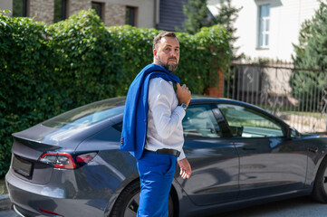 Attractive bearded man in a blue suit near a black car in the countryside in summer.