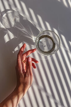 Female hand touching a glass of clear water, view from the top, white table, morning light