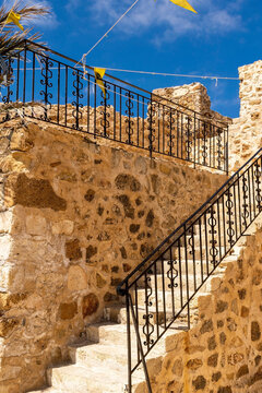 Stone ruined medieval steps. Yellow antique wall. Greek flags. Wrought iron railings