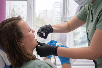 dentist applying invisible aligner on a female patient's teeth at a modern clinic, with the concept...