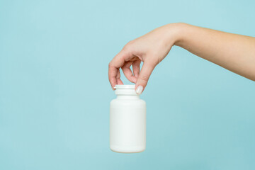 Woman's hand holds white plastic tube. Bottle for pill, capsule or supplement. Product branding...