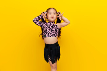 little asian girl in dance outfit dances chachacha on yellow isolated background, korean child dancer trains dance