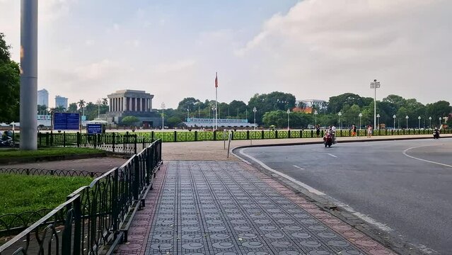Journey through Hanoi: Strolling on Sidewalk with Scenic Green Lawn and Vietnamese Flag"