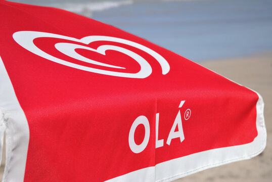 Guarda-sol com estampa de marca de gelados portuguesa, com ambiente de praia, mar em segundo plano, desfoque