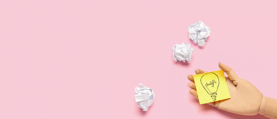 Wooden hand and paper with drawn light bulb on pink background with space for text. Insight concept