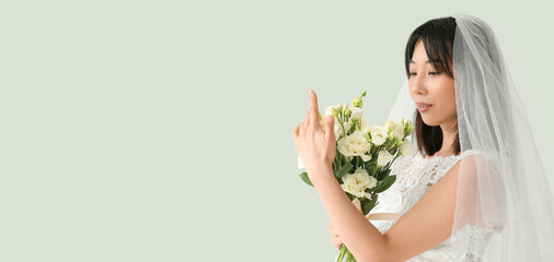 Fototapeta na wymiar Beautiful young Asian bride with bouquet of eustoma flowers on light background with space for text