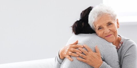 Happy elderly woman hugging her daughter at home