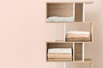 Shelf unit with beautiful sweaters near beige wall in room