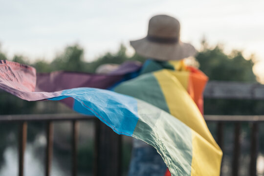 Unrecognizable young woman on her back leaning on a wooden bridge with a rainbow flag knotted around her neck waving in the wind. LGTBIQ+ Concept