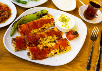 Fototapeta premium Portion of beyti kebab served on plate with grilled vegetables and yogurt.