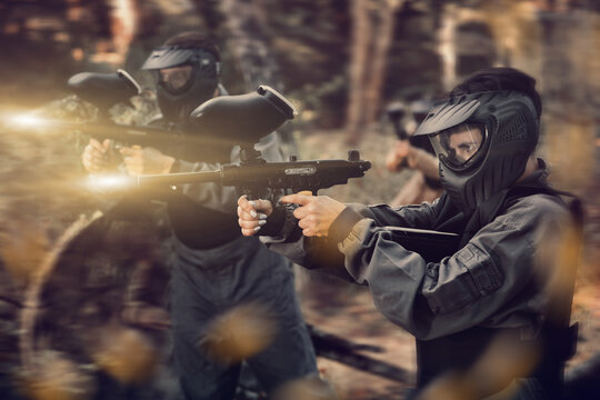 Woman targeting with paintball gun to eliminate enemies on battlefield. Team shooting with paintball markers.