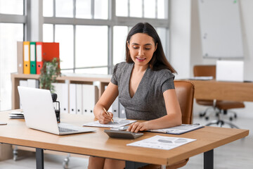 Female accountant working with calculator at table in office