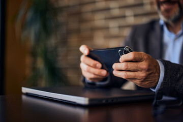 Close-up of a businessman's hands, holding a mobile phone and sitting in his office.