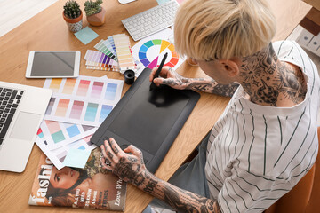 Tattooed graphic designer working with tablet on table in office, closeup