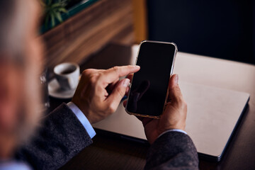 Man using a mobile phone, doing something over it, sitting indoors.