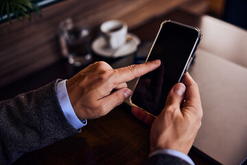 Focus on the male hands holding a mobile phone, sitting at the restaurant, drinking coffee.