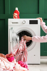 Woman putting dirty clothes in washing machine at home