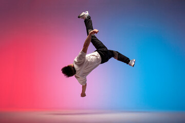guy acrobat doing back fat in new lighting, male dancer jumps and falls in the air on red blue...