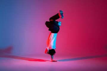 young guy dancer is dancing break in neon lighting, male acrobat is doing trick and dance exercise