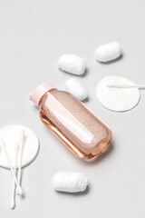 Bottle of micellar water with cotton balls, buds and pads on light background, closeup