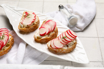 Plate with delicious radish bruschettas on white tiled table