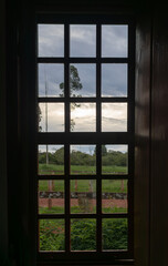 Wooden window overlooking fields and trees in a rural setting. Cloudy summer day make this a beautiful scene